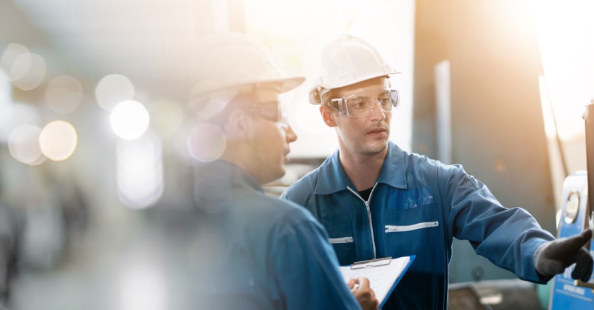 Two people in hardhats looking at a machine