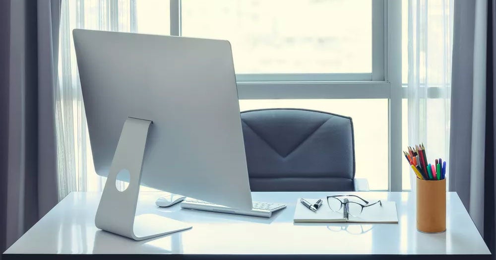 Computer, notepad, and pencil cup sitting on an empty desktop