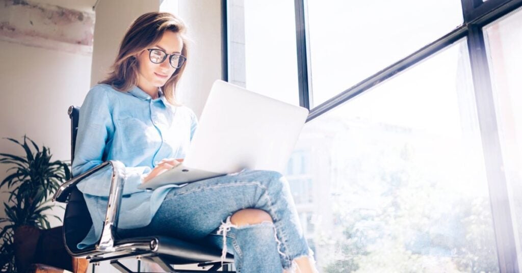 Woman sitting in a chair while reading a laptop