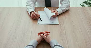 Two sets of hands on a wooden table with a notepad and pen