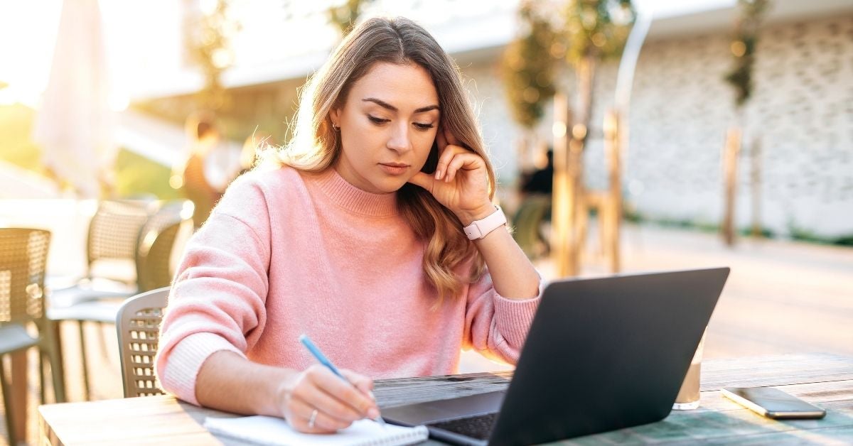 Woman taking notes in front of a laptop