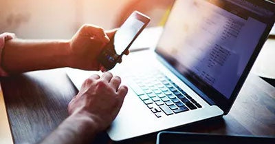 Hands holding a smartphone and a laptop