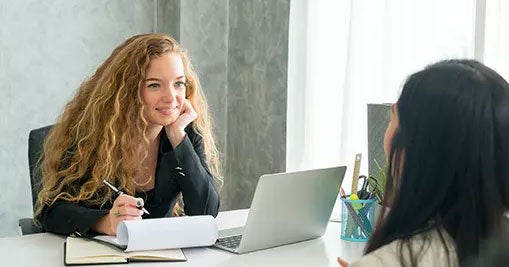 Woman with pen and notepad sitting across the table from another person