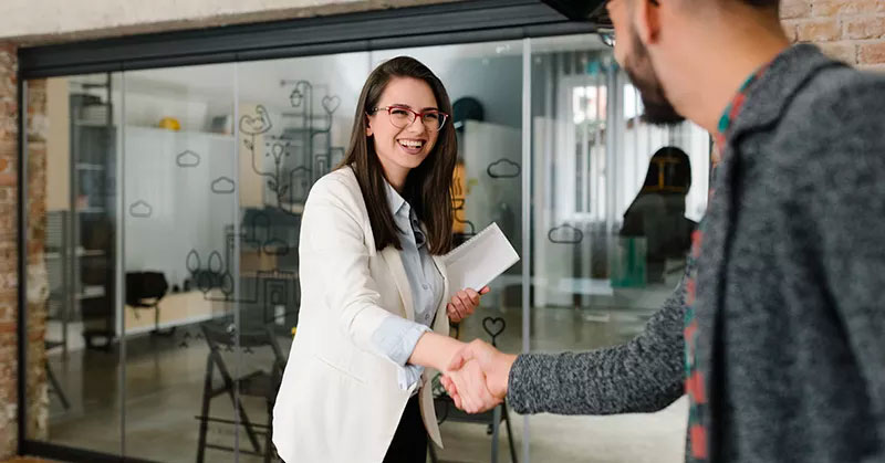 Woman shaking hands with another person in front of a glass office door