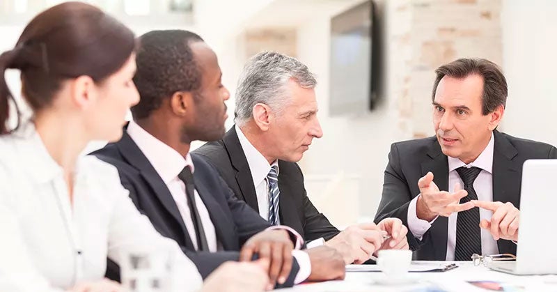 Four people in suits talking around a white table