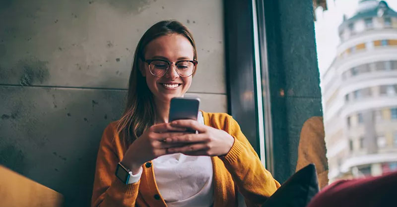 Women in a yellow cardigan smiling at her smartphone