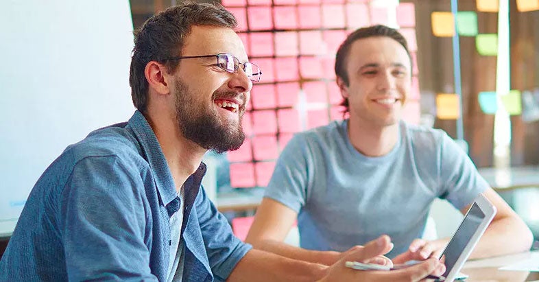 Two men smilling in front of a wall of post-it notes