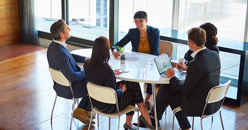 Five people in suits gathered around a small table