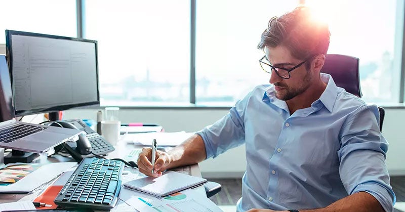 Man taking notes by hand at a messy desk