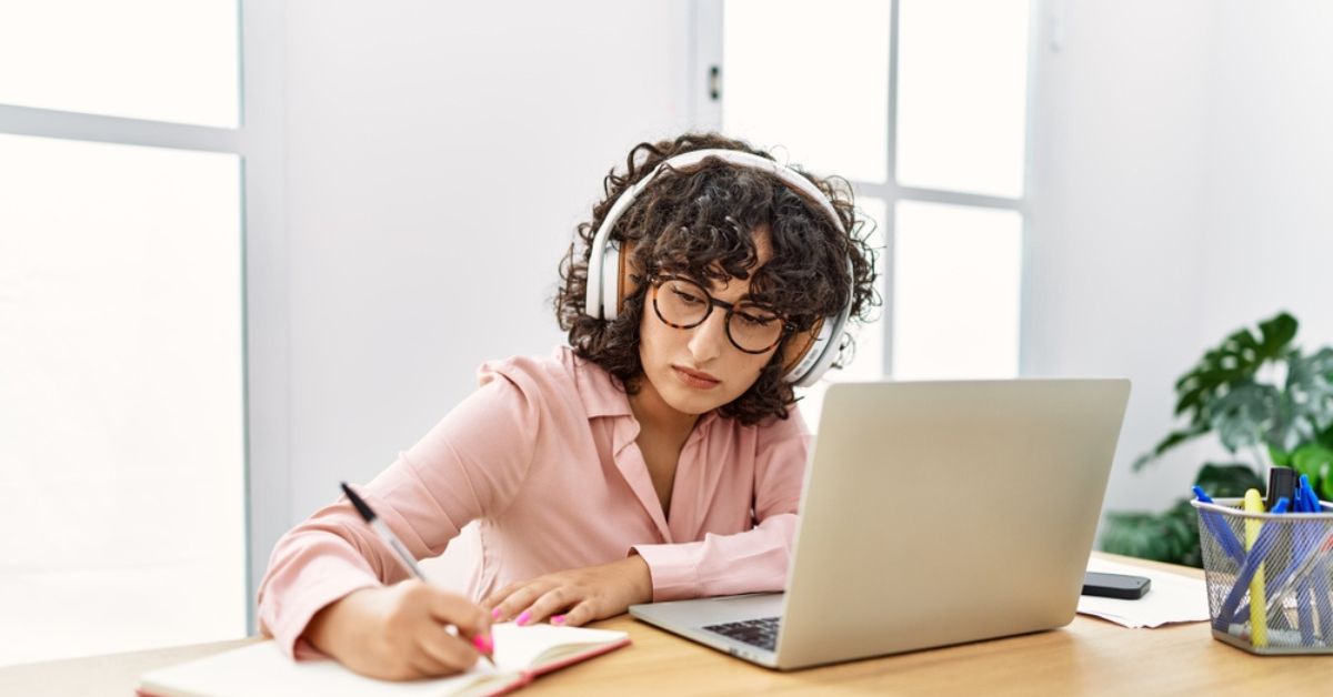 Woman wearing headphones taking notes