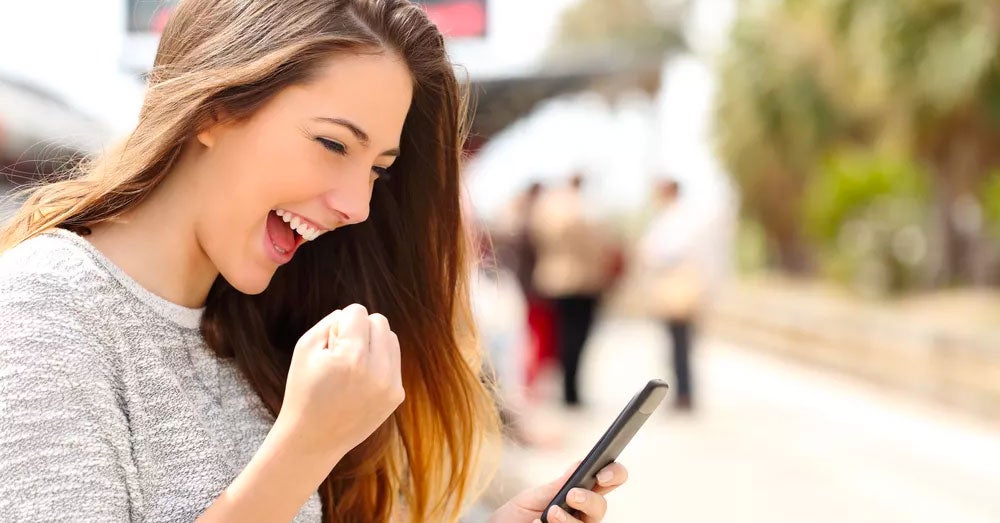 Excited woman pumping her fist while reading news on her smartphone