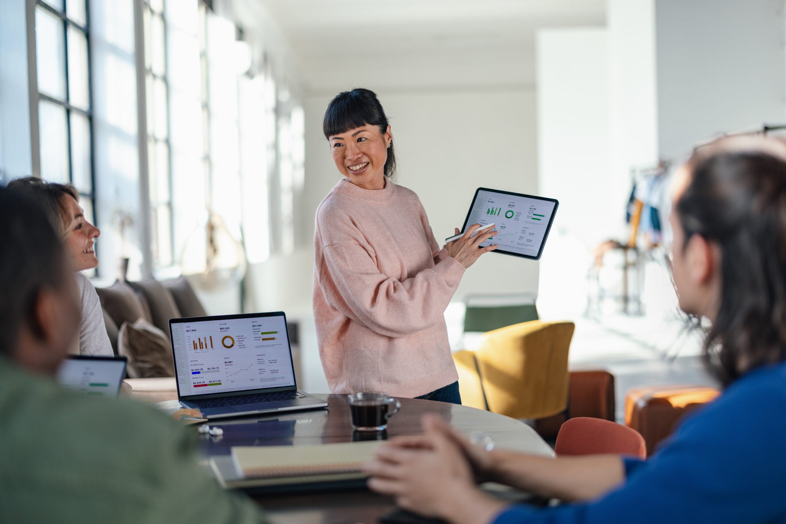 A team of young professionals collaborating in a modern workspace, discussing data displayed on laptops and a tablet. Ideal for themes of teamwork, innovation, and digital technology.