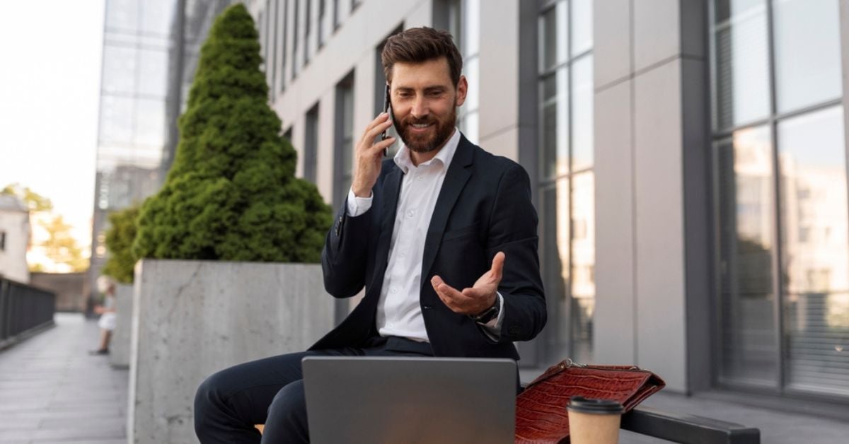 Man on a phone waving towards a laptop