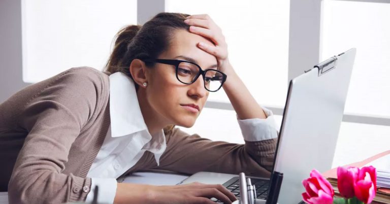 Woman slumped onto her desk looking at a laptop
