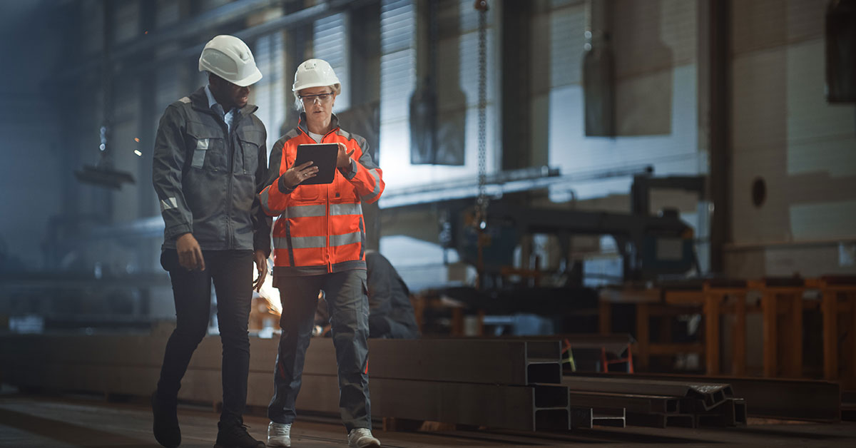 Two people wearing hardhats standing on a factory floor