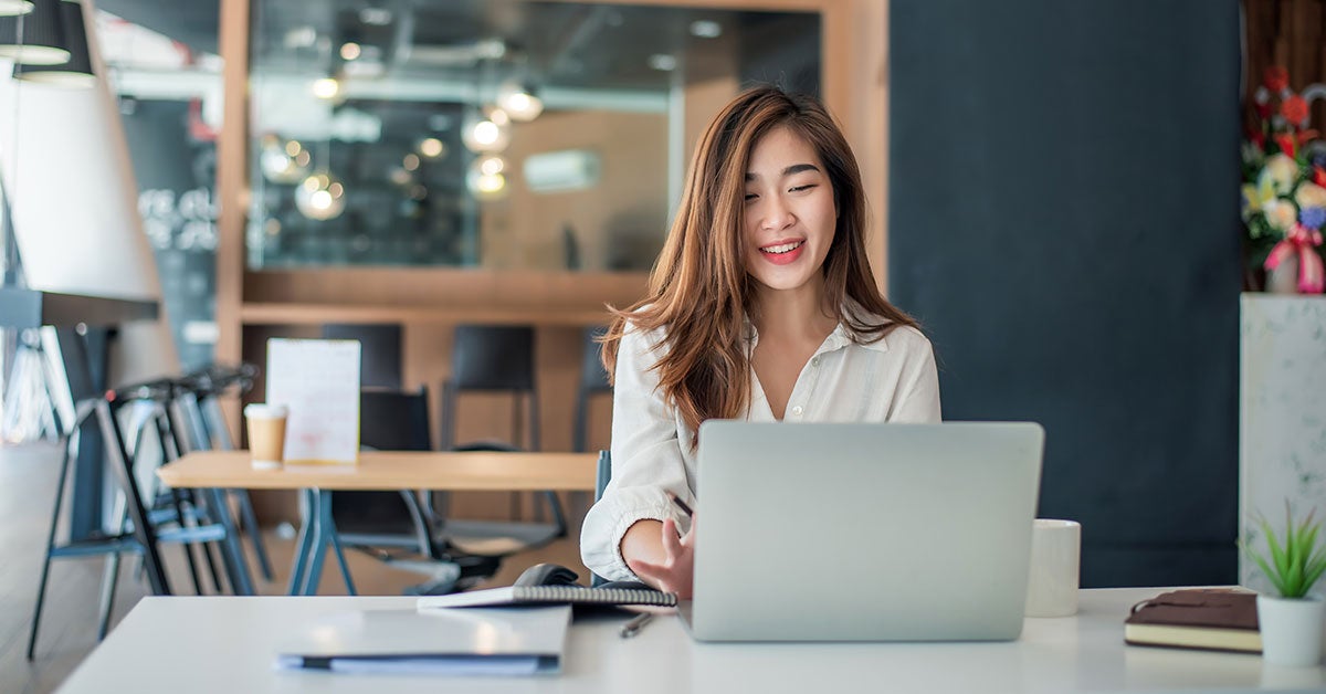 Woman sitting at a white desk typing on a laptop