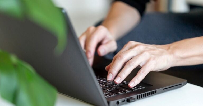 Two hands typing into a laptop keyboard