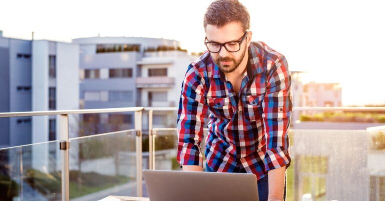 Man standing on a balcony looking at a laptop