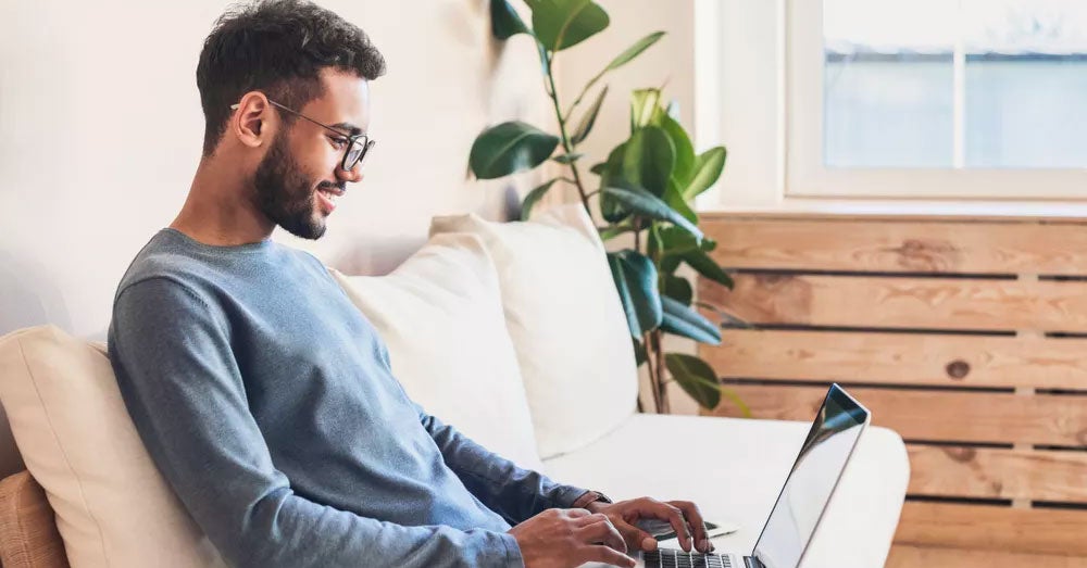 Man sitting on a cream sofa typing on a laptop