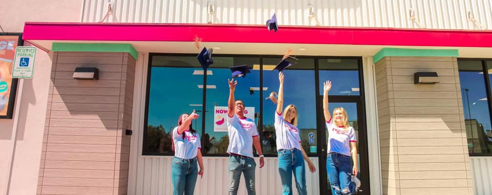 Four eegee's employees tossing graduation caps in the air