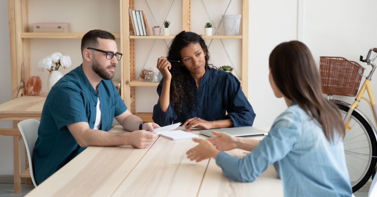 Two people talking to a candidate at a wooden table