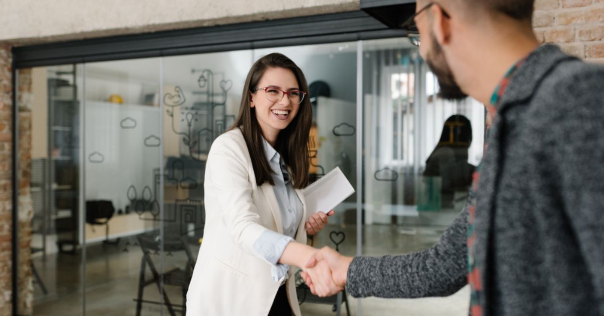 Professional woman shaking hands with another person in a glass office