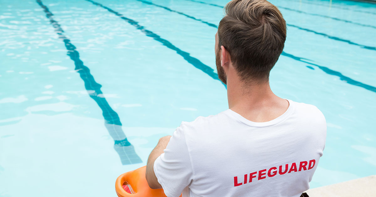 Person in a lifeguard shirt sitting in front of a swimming pool