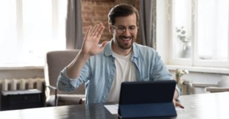 Man in glasses smiling and waving to someone on a virtual call on a tablet
