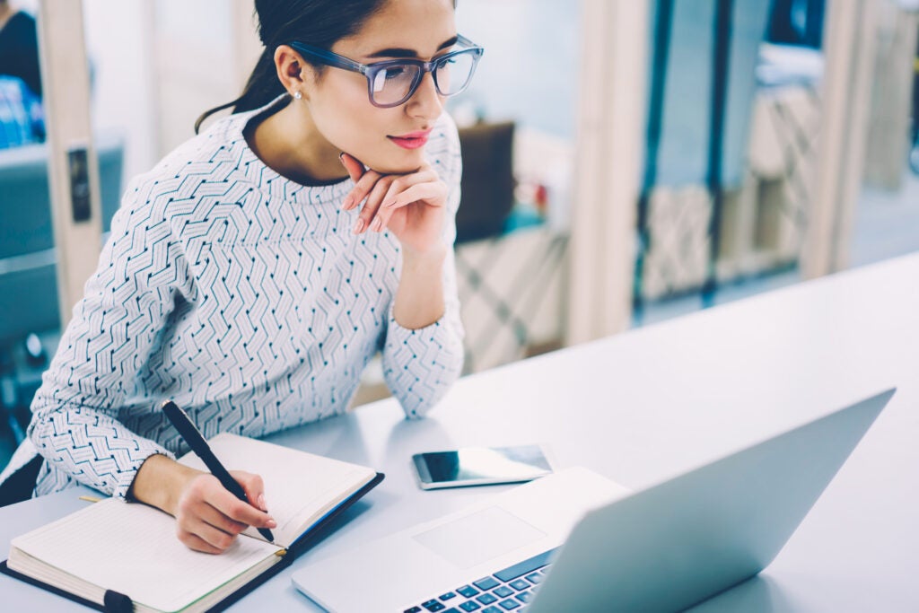 Woman taking notes while looking at a laptop