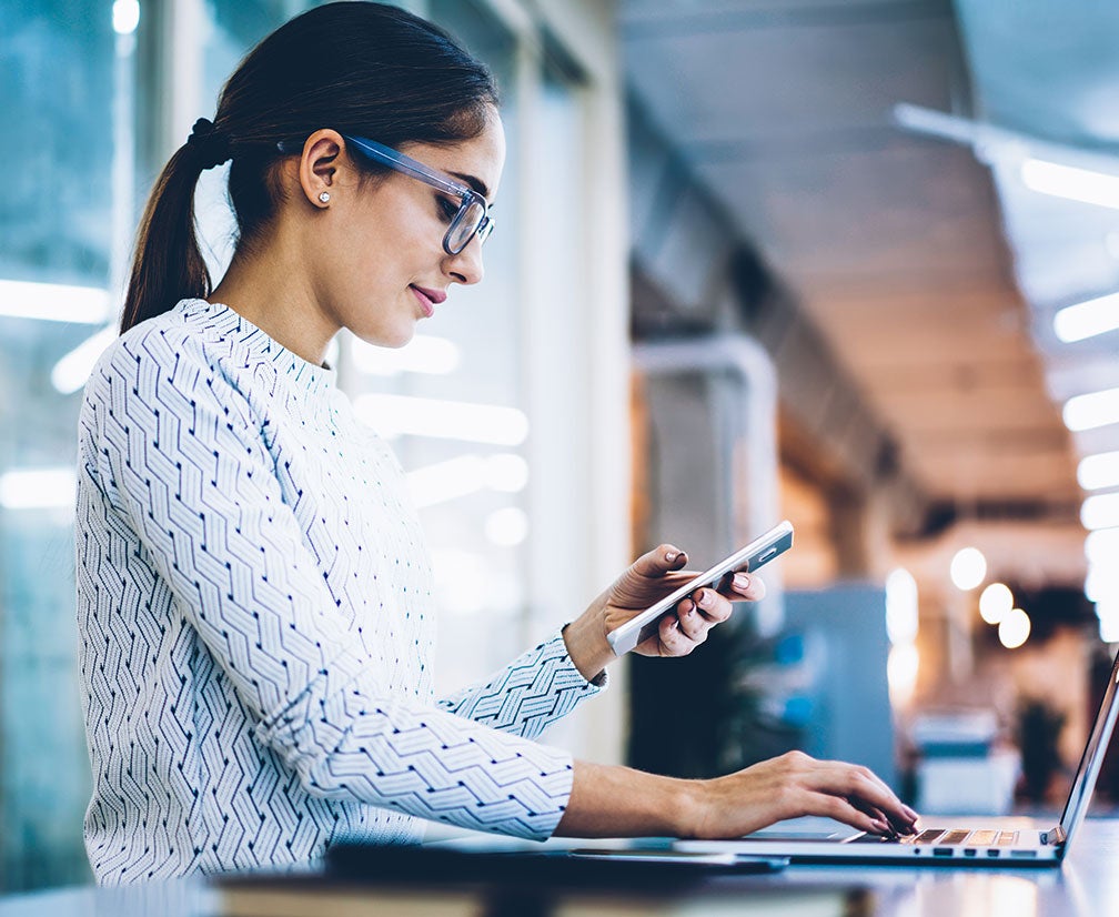 A woman using both a laptop computer and a cell phone