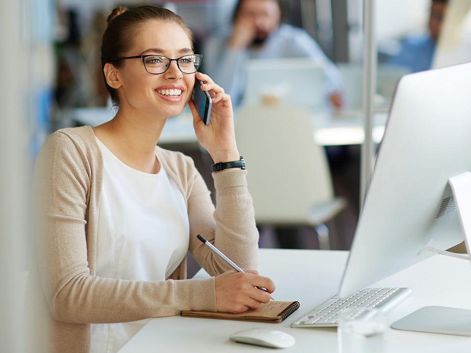 Woman in glasses smiling on a phone at a desk