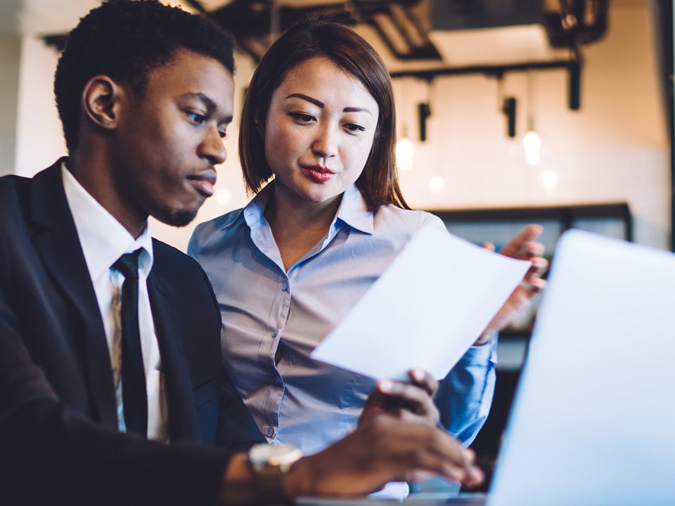 Man in a suit and a female colleague look at a laptop together