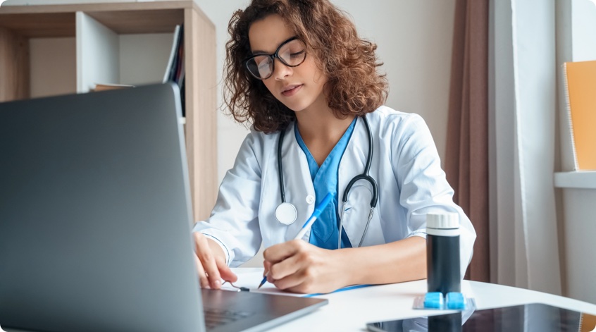 Medical professional taking notes in front of a laptop