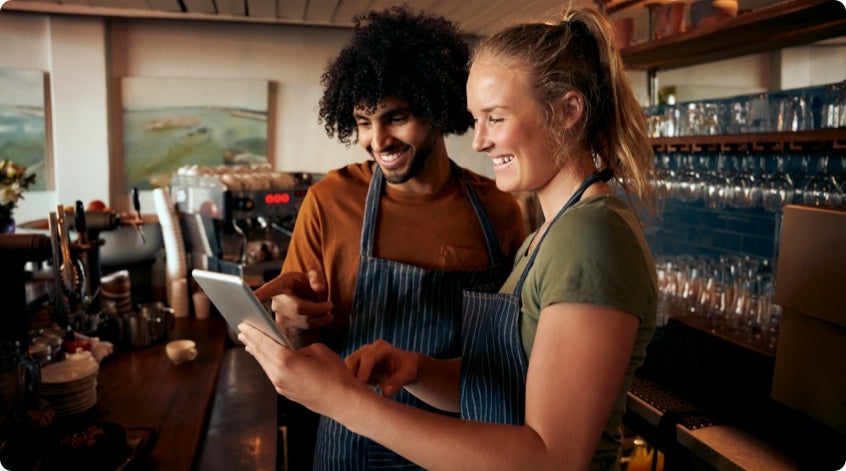 Two baristas in a coffee shop laughing over a tablet