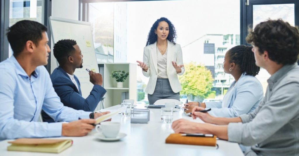 Woman presenting ideas to four people sitting around a conference table