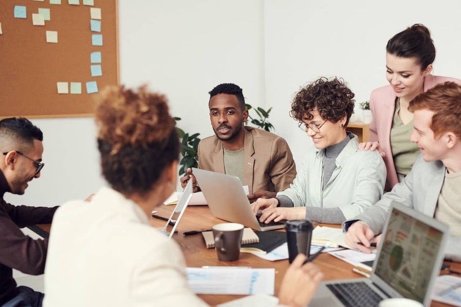 Employees of many different backgrounds place their hands together in a gesture of teamwork