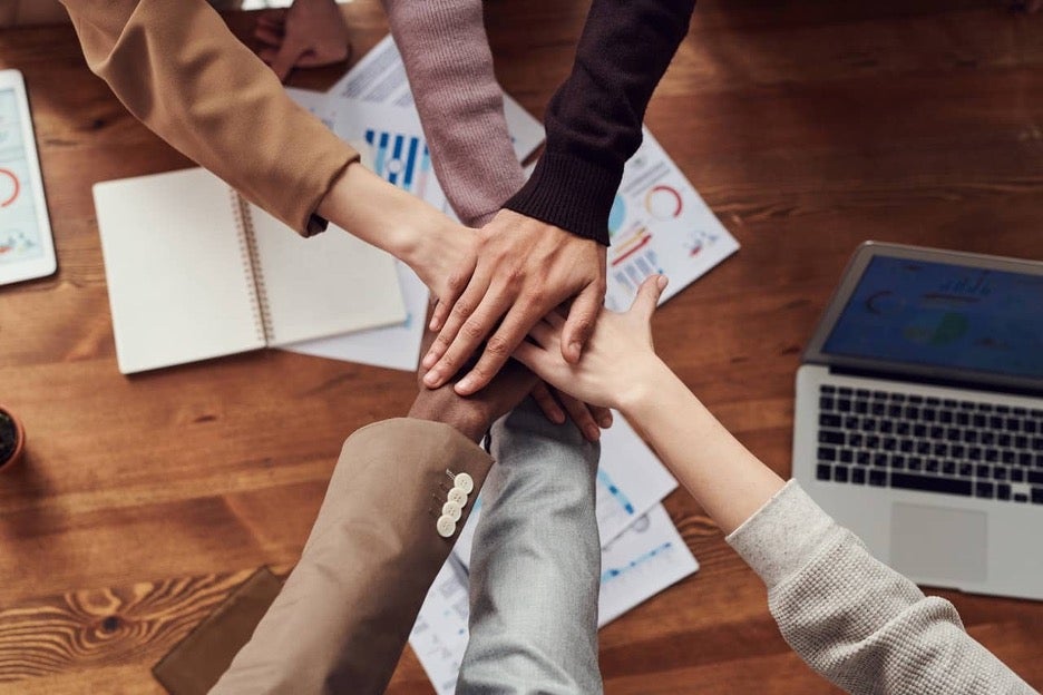 Employees of many different backgrounds place their hands together in a gesture of teamwork