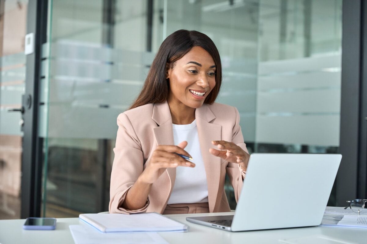 Young professional woman sitting at desk taking video call on laptop