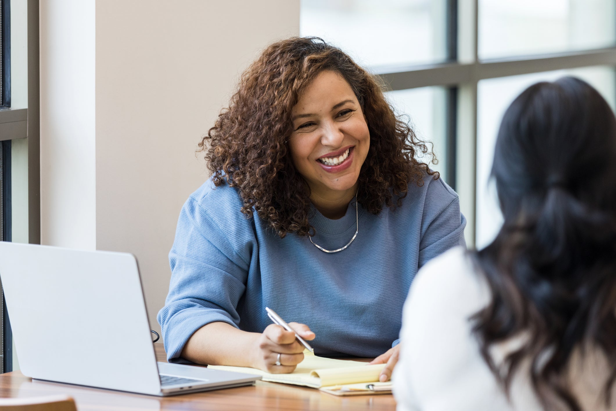 The mature adult female business owner smiles encouragingly at an unrecognizable female job applicant.