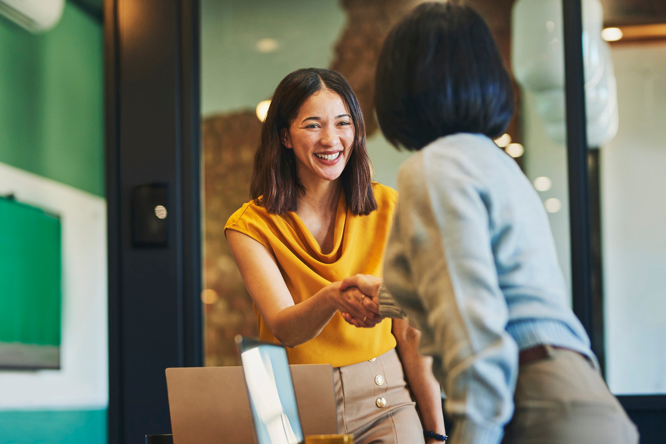 Businesswoman shaking hands with client and smiling cheerfully in meeting room.